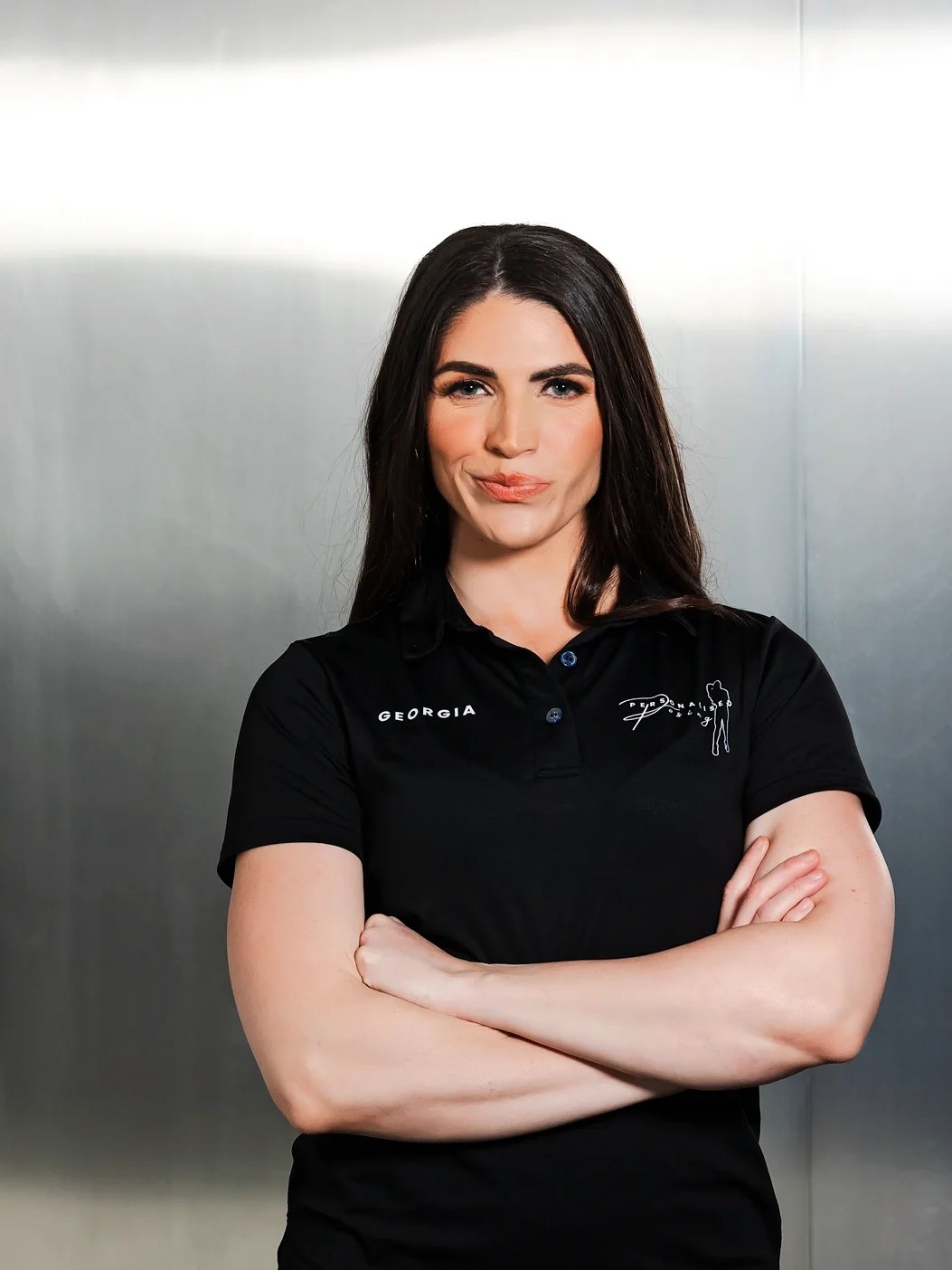 Georgia Voice standing arms-crossed against a steel wall in her Personalised Posing polo
